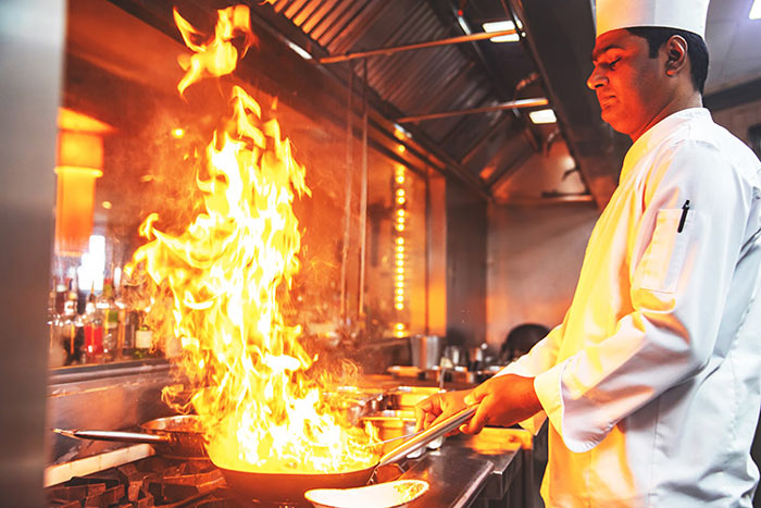 chef holding flaming pan in kitchen