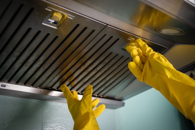 Worker cleaning a commercial kitchen hood filter while wearing gloves in Goldsboro, NC