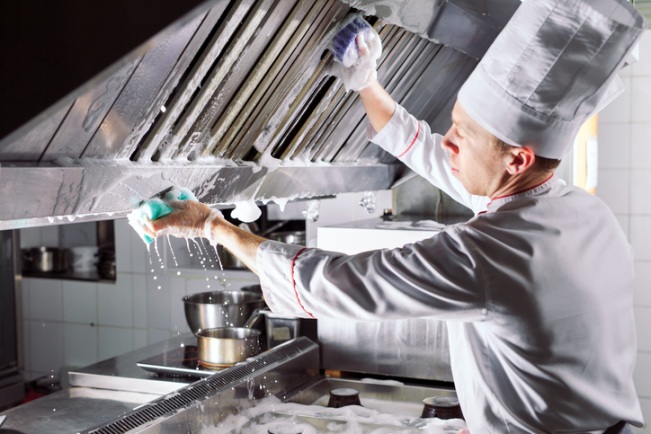 Kitchen staff scrubbing grease from a commercial exhaust hood during cleaning in Fayetteville, NC